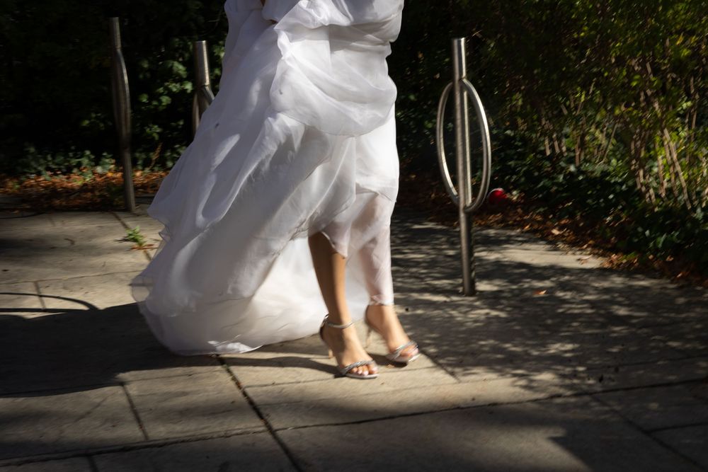 Close-up view of flowing white wedding dress hem and bare feet on stone patio in dappled sunlight.