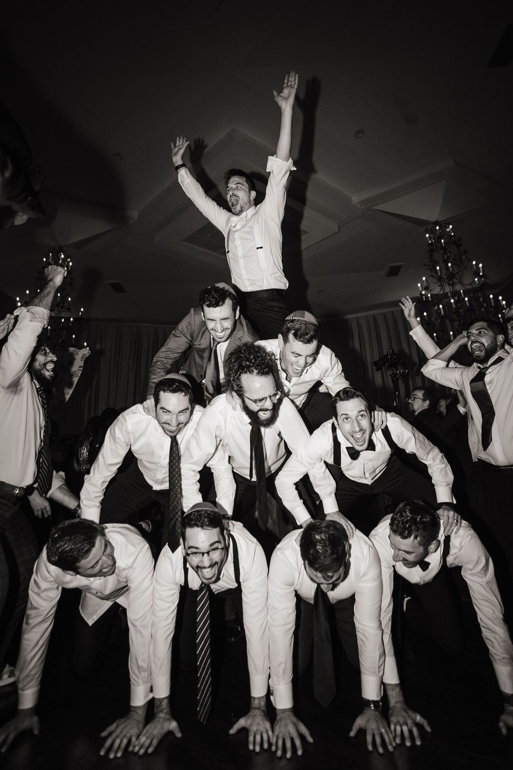 Wedding guests form a human pyramid on the dance floor during a black and white reception celebration.