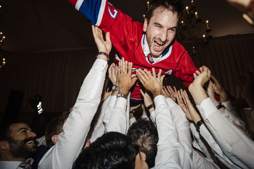 Celebratory moment of a hockey player being lifted up by teammates wearing white jerseys at an indoor venue.