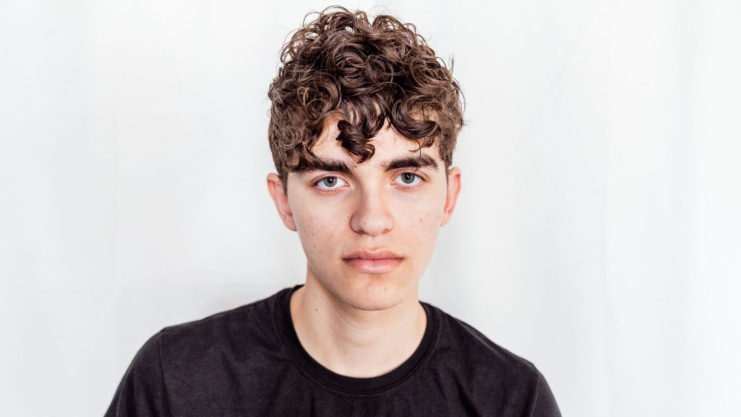 Studio portrait against white background featuring curly hair and black t-shirt.
