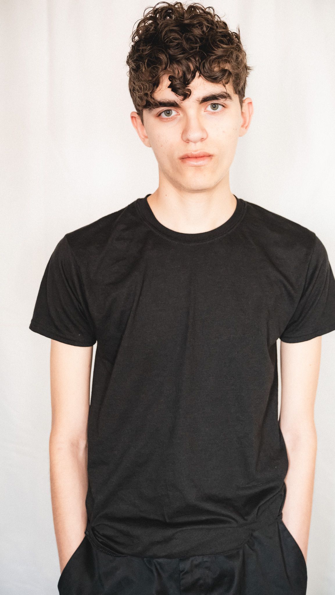 Fashion photography of person in black t-shirt against white backdrop.
