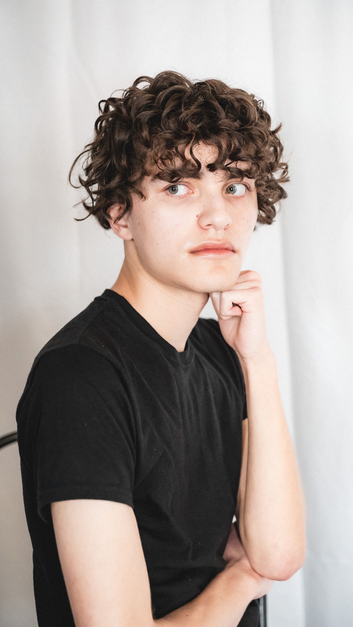 Portrait with curly hair against white background in contemplative pose.