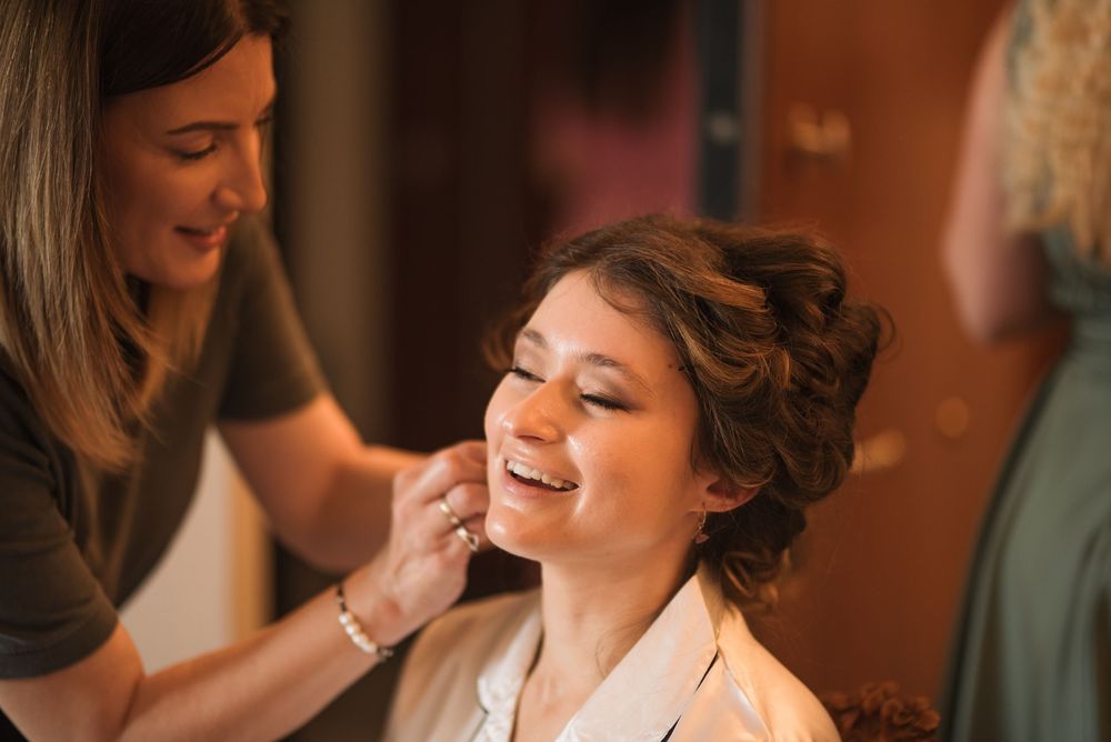 Candid moment of bride getting her makeup done while wearing white getting-ready robe.