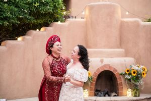 Same sex couple sharing a joyful moment together beside an adobe style wall with a decorative fireplace and sunflowers at El Zocalo Plaza.