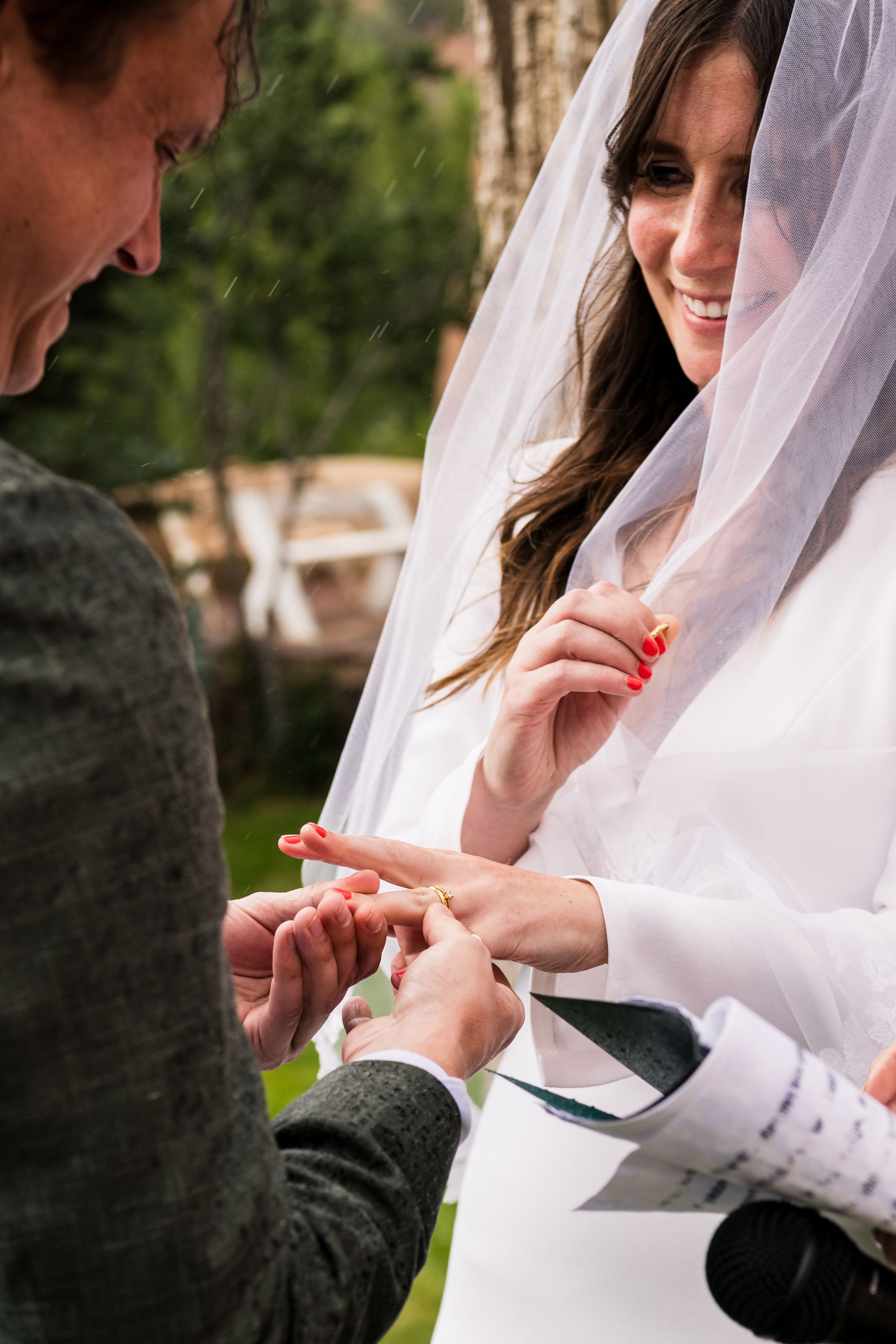 Close-up sequence of exchange of wedding rings during outdoor marriage ceremony with bride wearing white gown.
