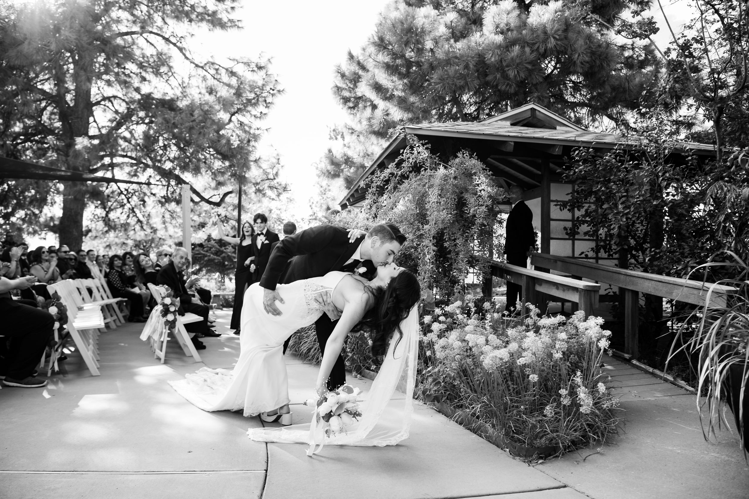 A joyful couple dips and embraces during their first dance at an outdoor garden wedding reception.