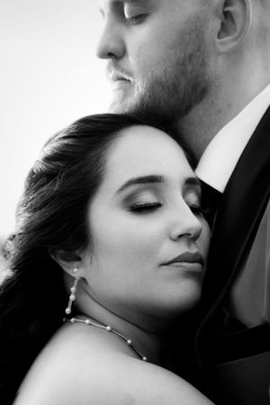 An intimate black and white portrait of a couple in formal attire sharing a tender moment.