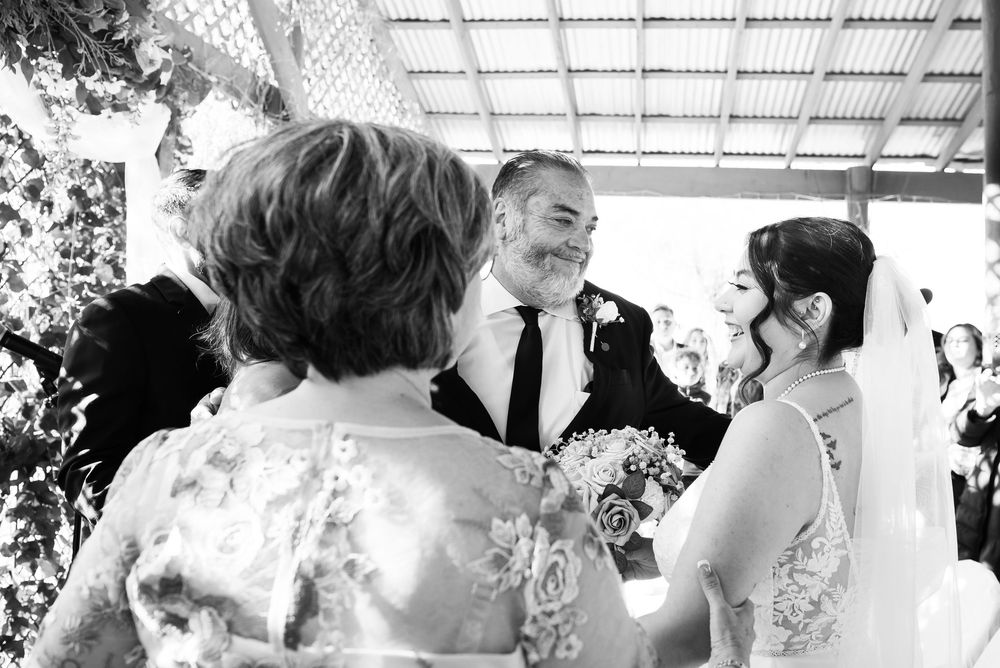 Black and white photograph of people celebrating and laughing during an outdoor gathering under pergola lighting.