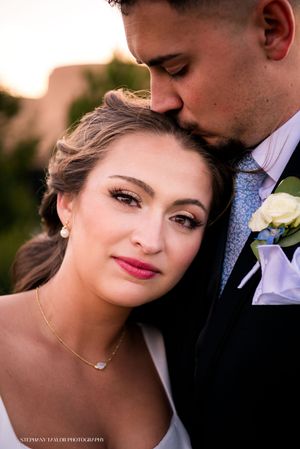 A romantic wedding portrait of a couple embracing in soft sunset lighting with elegant formal attire and floral details.