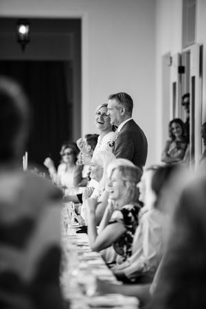 Black and white photo of wedding reception guests laughing and enjoying the speeches during dinner festivities.