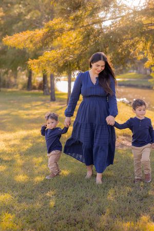 A family in navy blue outfits walks together through a sunlit field with golden autumn foliage in the background. In Houston, TX