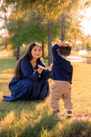 Person in navy blue sweater lying on autumn grass during golden hour sunset in park setting. In Houston, TX