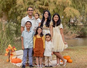 A group gathers outdoors for fall family photos with orange pumpkins and rustic autumn decor in a natural setting.