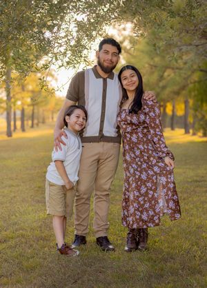A family enjoys a warm autumn day together in a sunlit park with golden trees in the background.