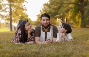 A family lies together on grass during golden hour sunset in a park setting.