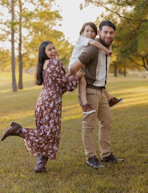 A family plays and poses together in a park during golden hour with fall trees in the background.