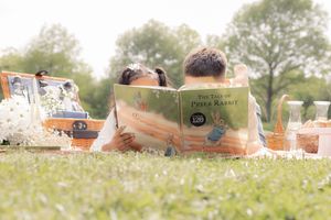Outdoor reading time during picnic. Brother and sister lying down and sharing stories.