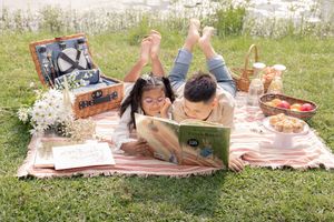 Outdoor reading time during picnic. Brother and sister lying down and sharing stories.