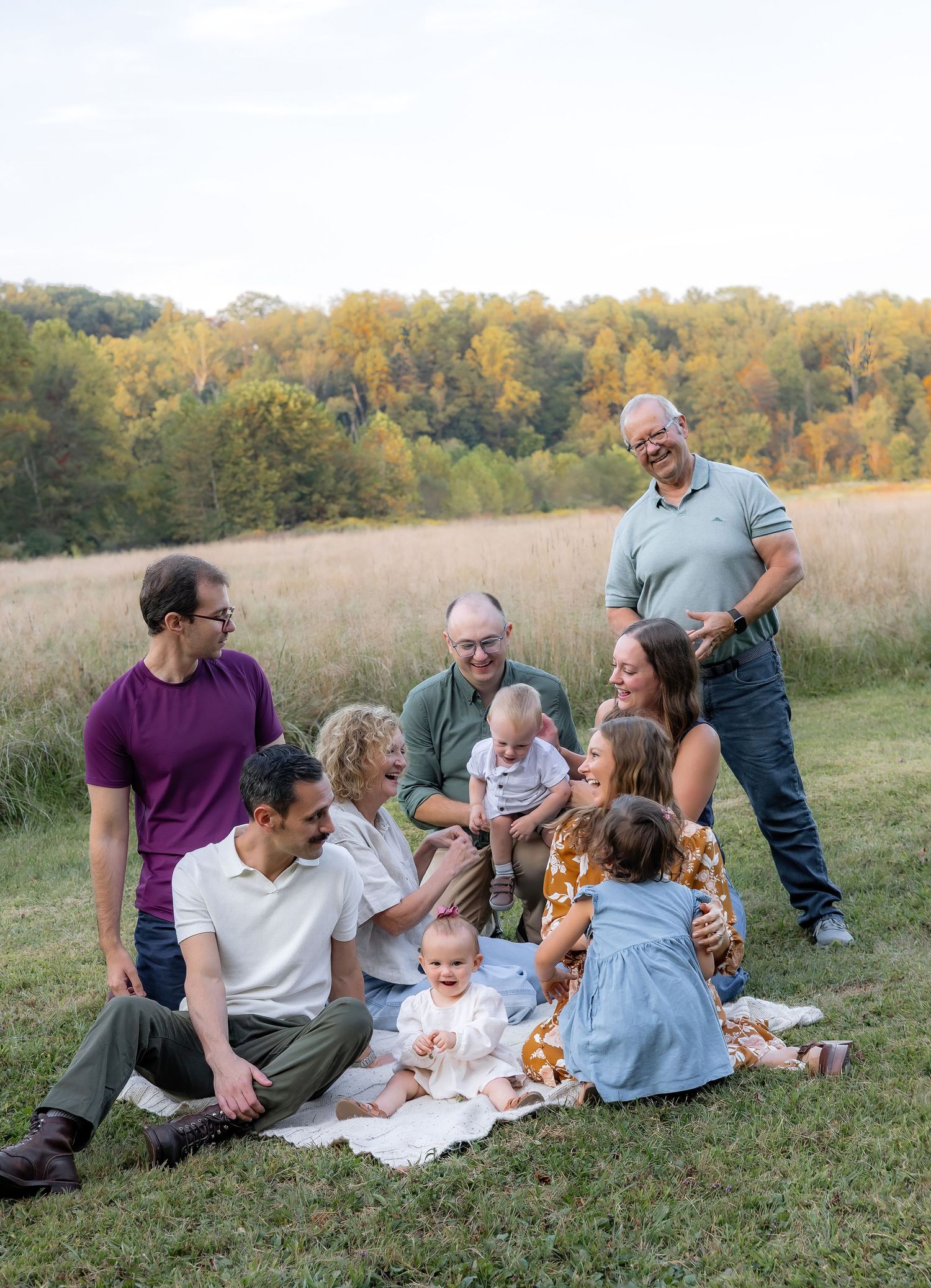 A group relaxes together on a grassy hillside during a sunny autumn afternoon in a casual outdoor setting.