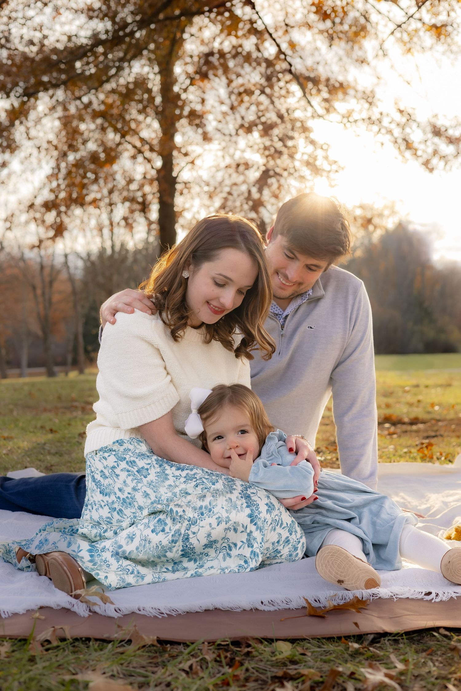 Family laying on blanket in autumn park during golden hour sunset photo session.