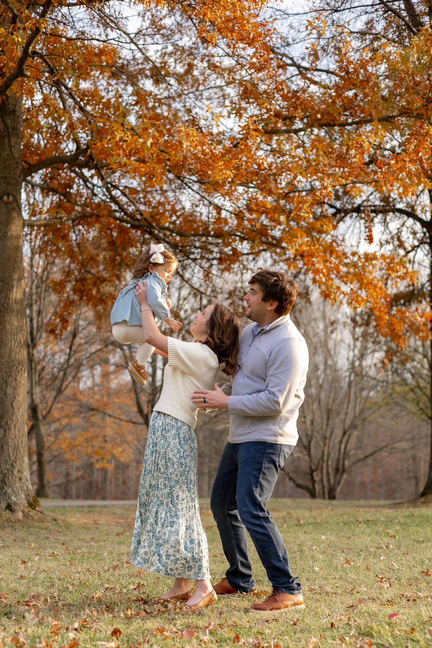 A couple dances together under vibrant orange autumn foliage in a park setting during fall.