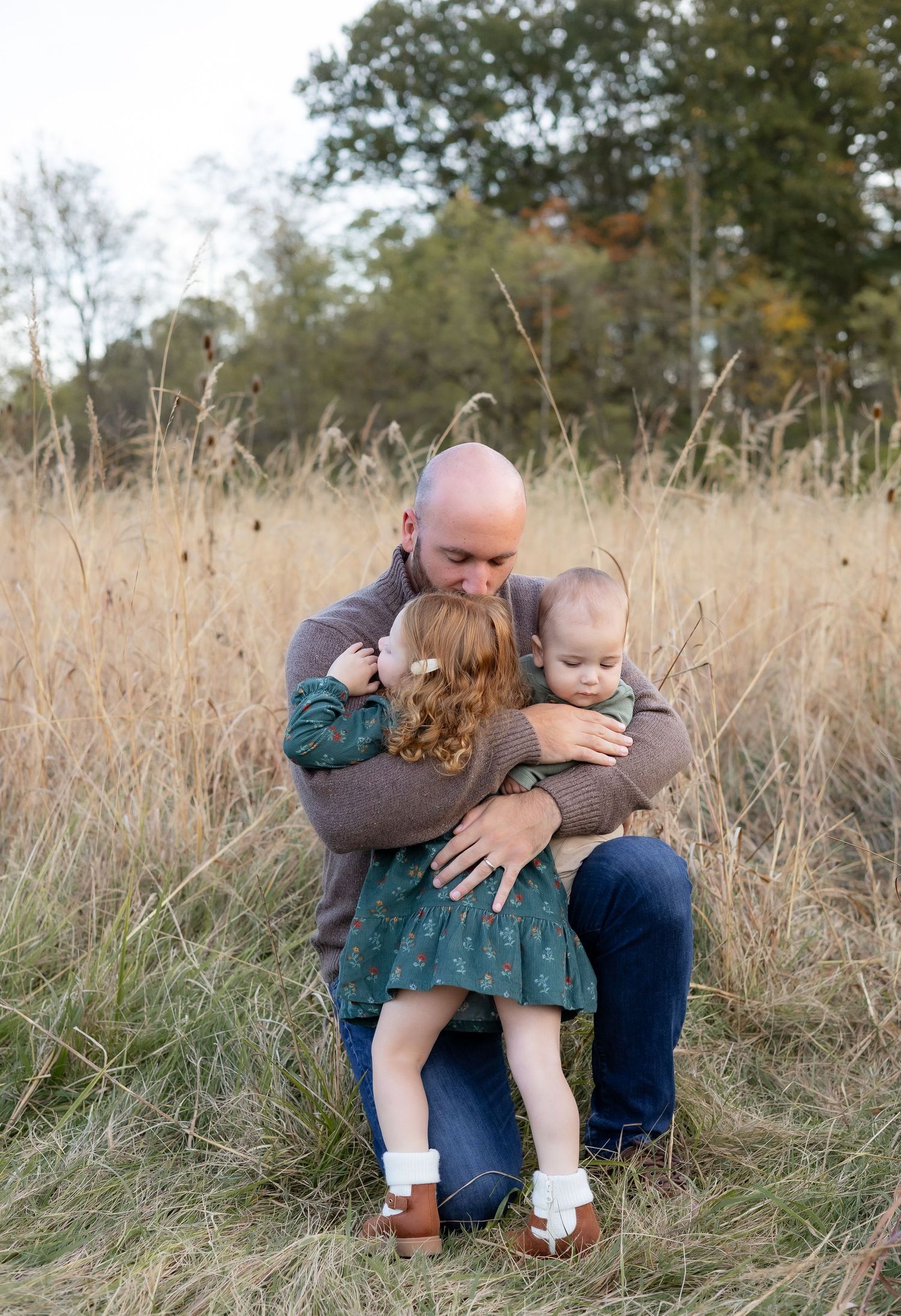 Family shares tender moments together while sitting in a tall grass field on an autumn afternoon.