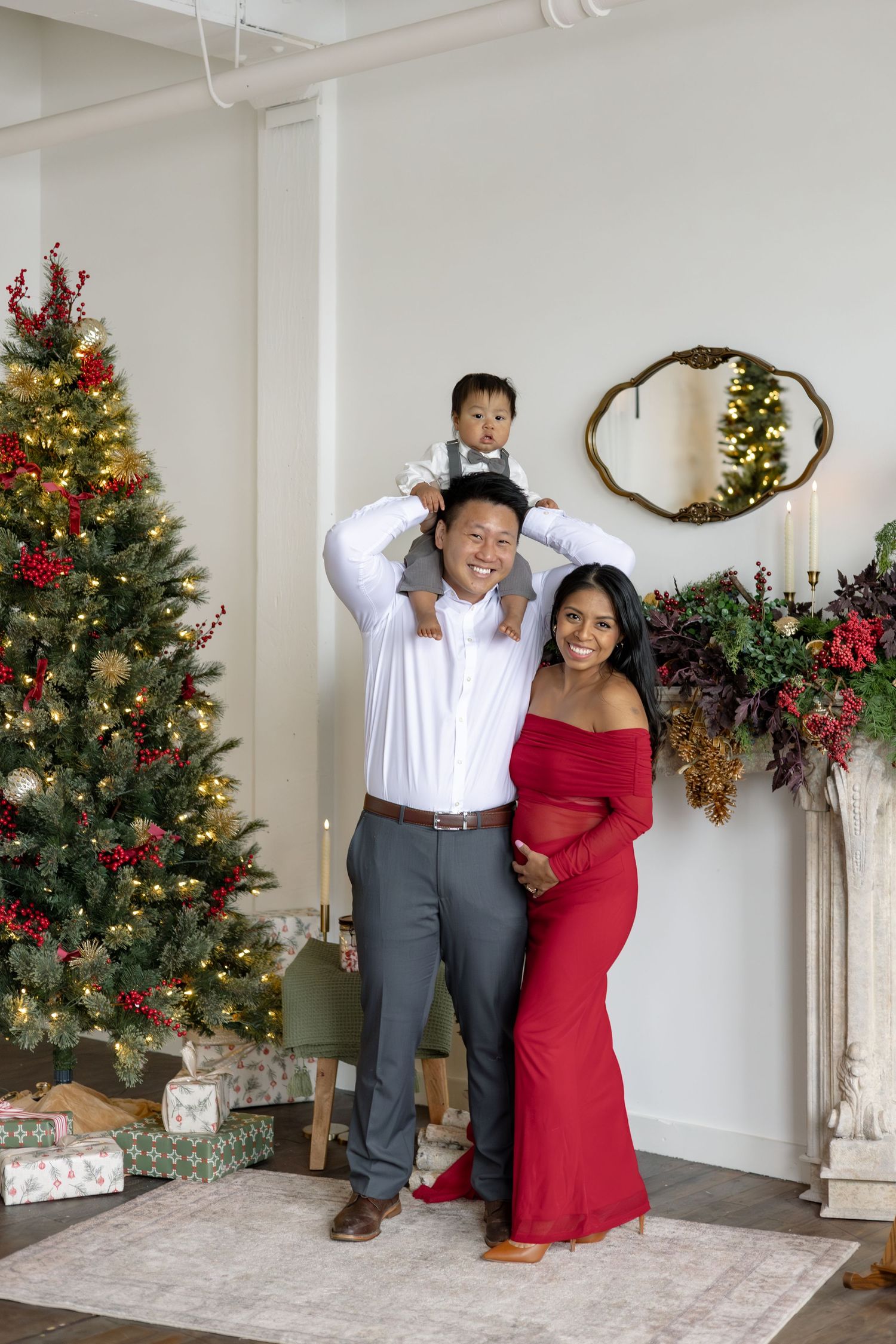 Couple poses playfully in front of decorated Christmas trees and holiday decor in a bright white room.
