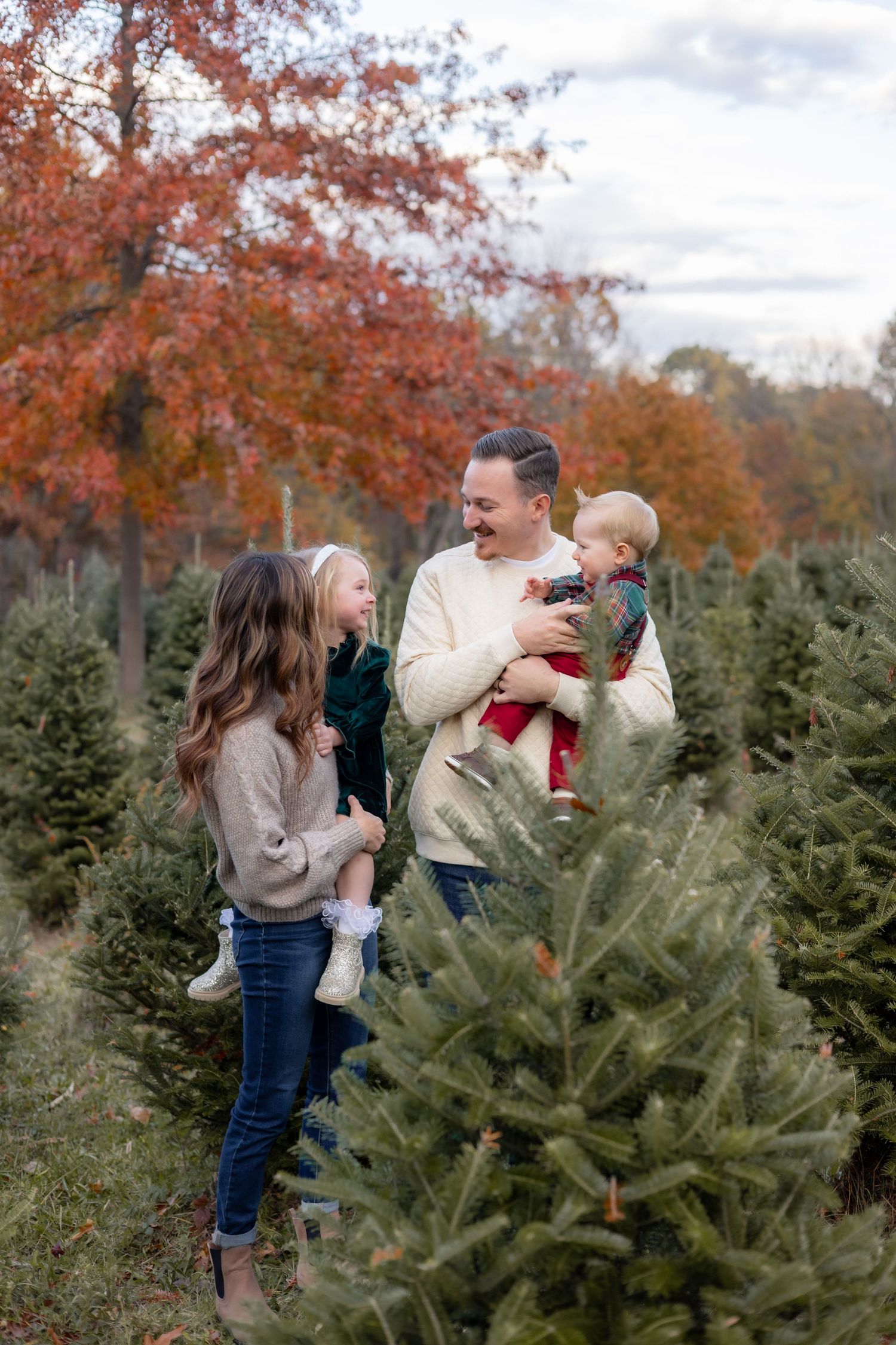 A family shares joyful moments together while shopping for Christmas trees among evergreens and autumn foliage.