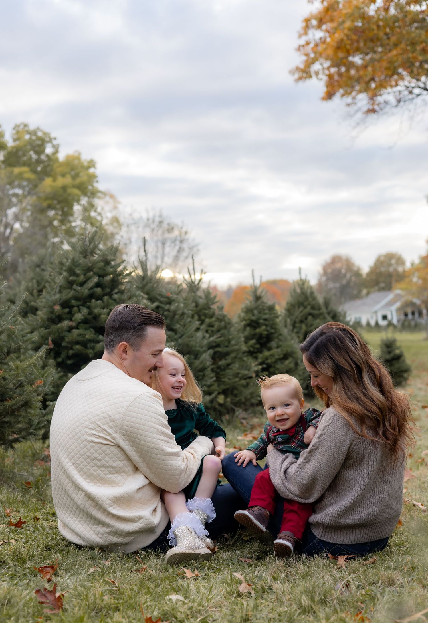 A family sits together on the grass at a Christmas tree farm on an autumn day.