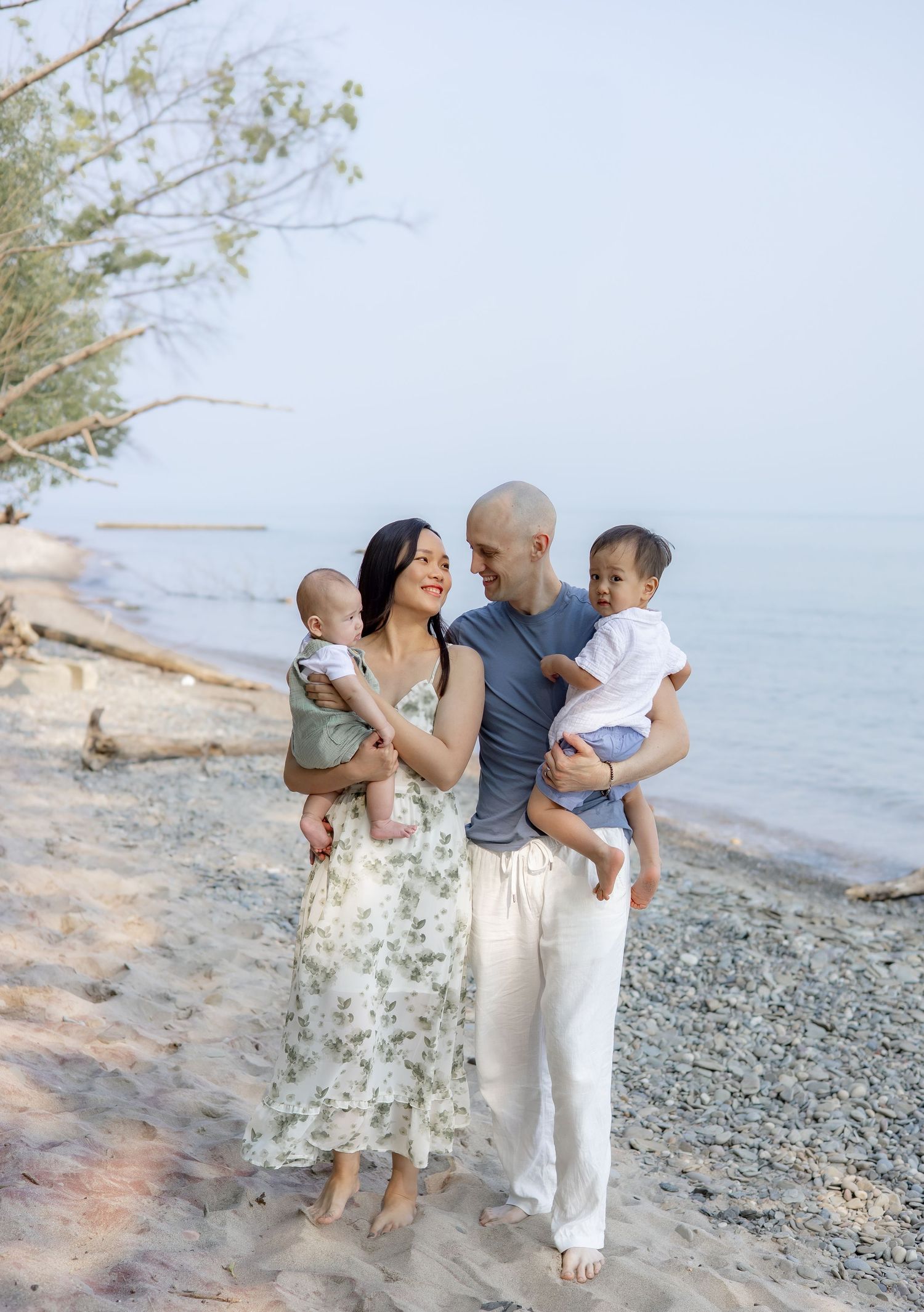 A family shares tender moments together on a rocky beach during a sunset photoshoot by the water.