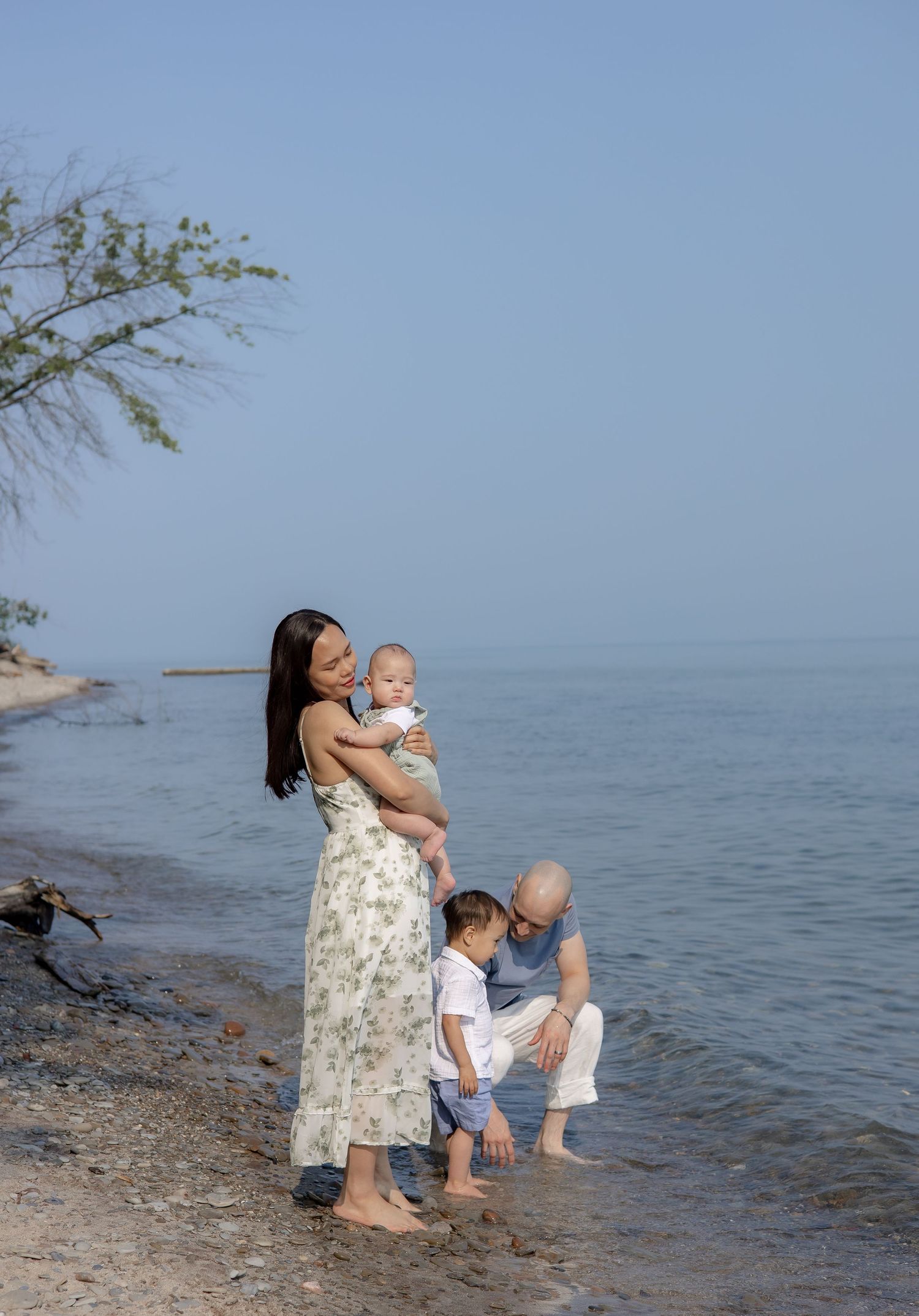 A mother and baby share a tender moment at the beach while sitting near the water's edge.