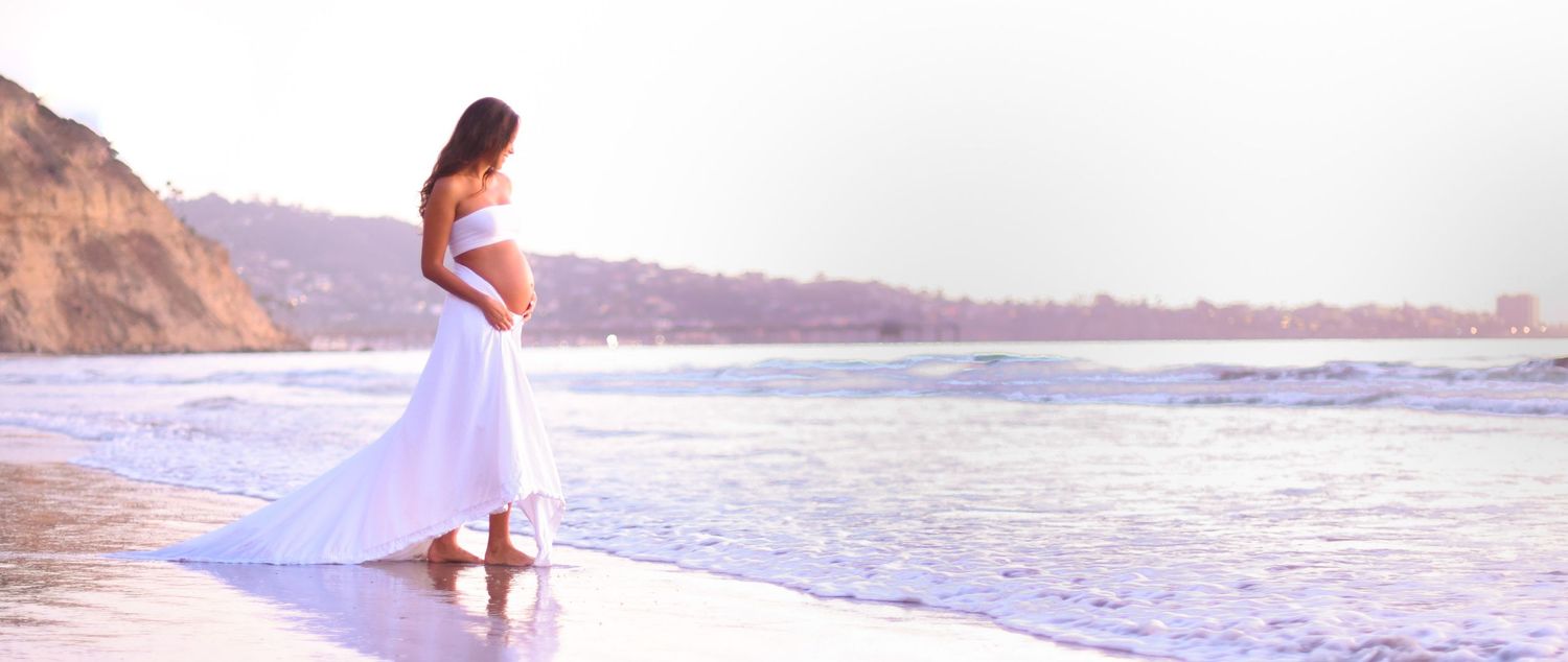 Person in flowing white dress walking along scenic coastal beach.