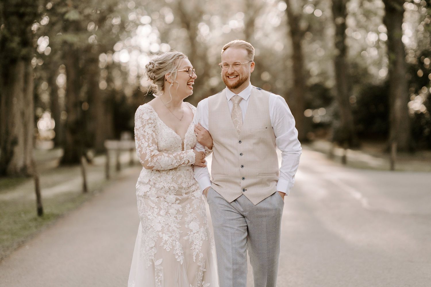 Romantic couple walking together on a tree-lined path in soft evening light.