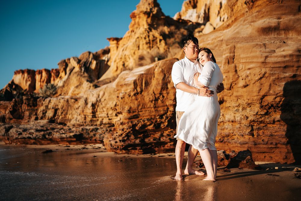 Couple with scenic coastal cliffs at sunset with golden light illuminating the rocky shoreline taken by Melbourne couples photographer.