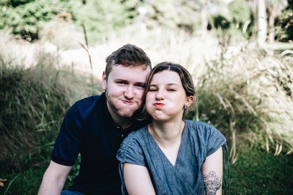 A sweet couple poses together outdoors in nature making playful expressions with grassy meadow taken by Melbourne couples photographer
