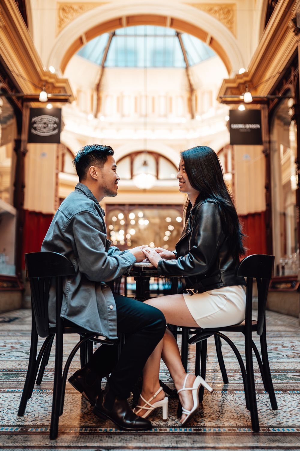 A couple shares a moment at a cafe table inside an ornate historic arcade with elegant architecture taken by Melbourne couples phographer.