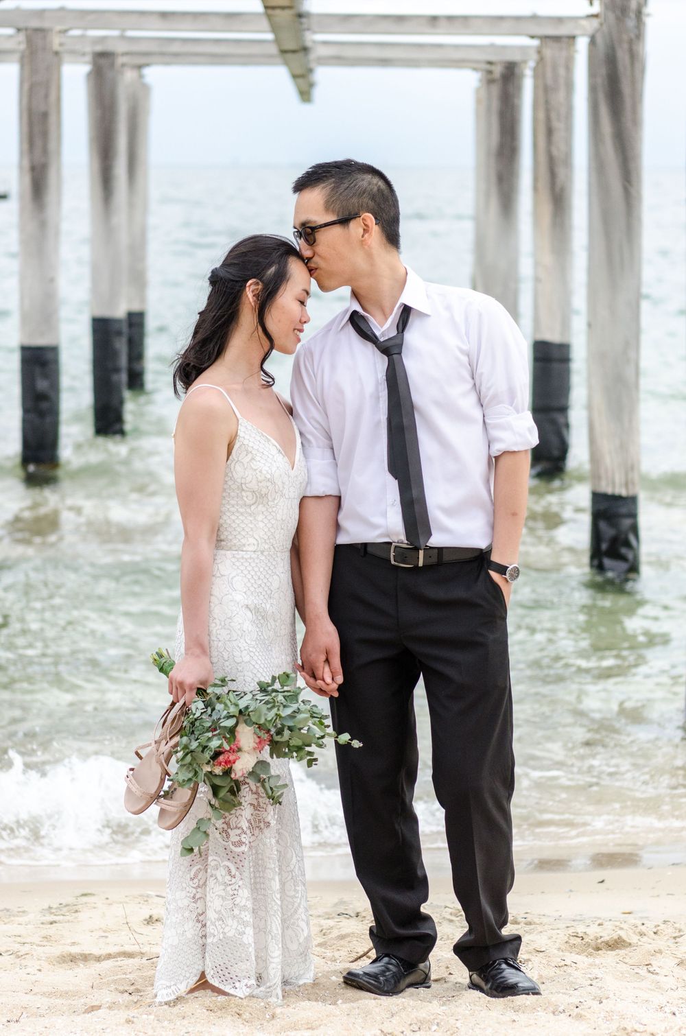 Beach pre-wedding portrait with couple near ocean shore with bridal bouquet taken by Melbourne couples photographer.