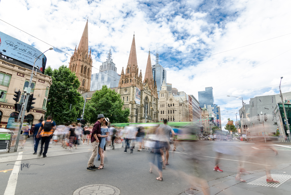 Motion blur of pedestrians walking past St Pauls Cathedral in Melbourne with a couple kissing taken by Melbourne couples photographer