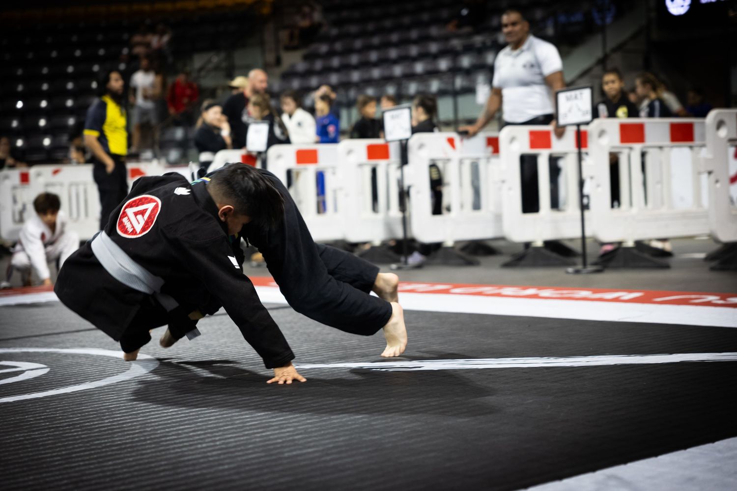 Martial artists demonstrate ground fighting techniques on black competition mats.