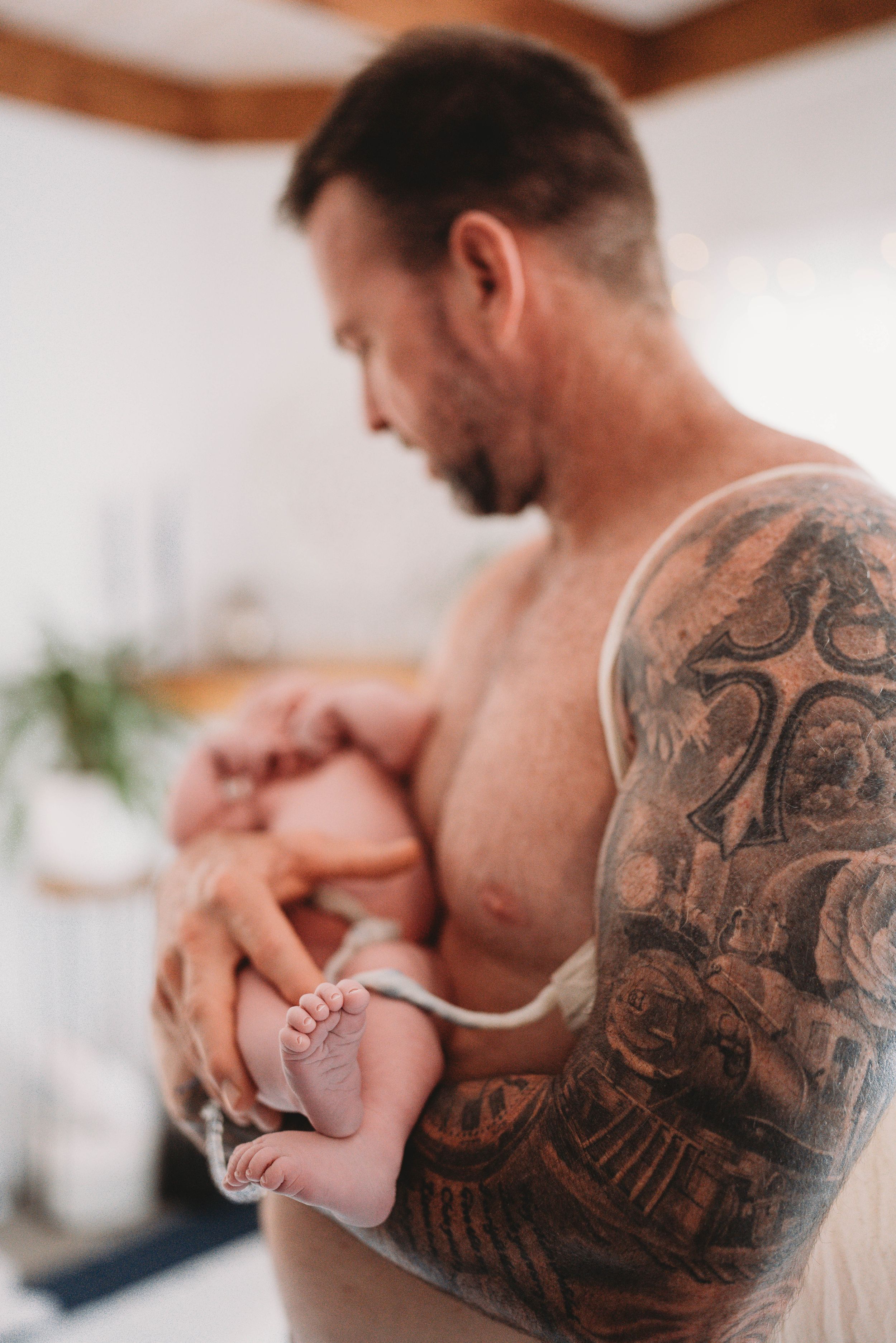Palm Beach newborn father with detailed sleeve tattoo gently holding tiny newborn feet.