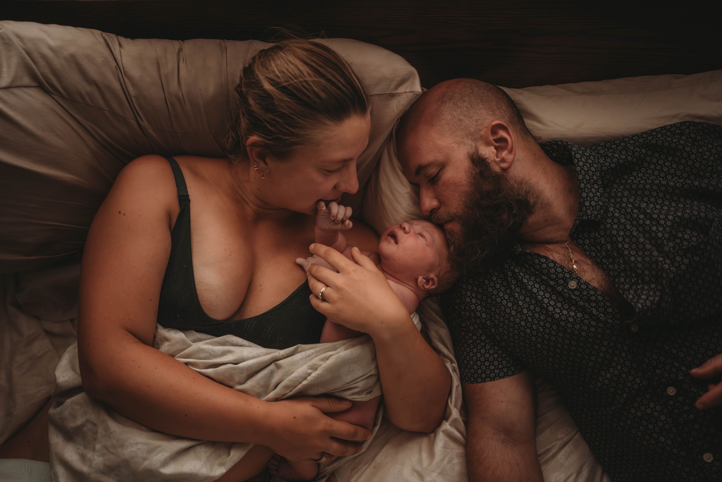 Intimate Palm Beach family moment with newborn baby lying between parents on bed.
