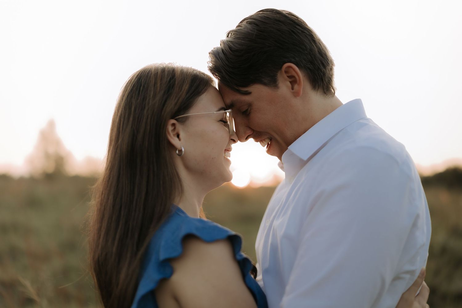 An intimate moment between a couple touching foreheads at sunset in a field.