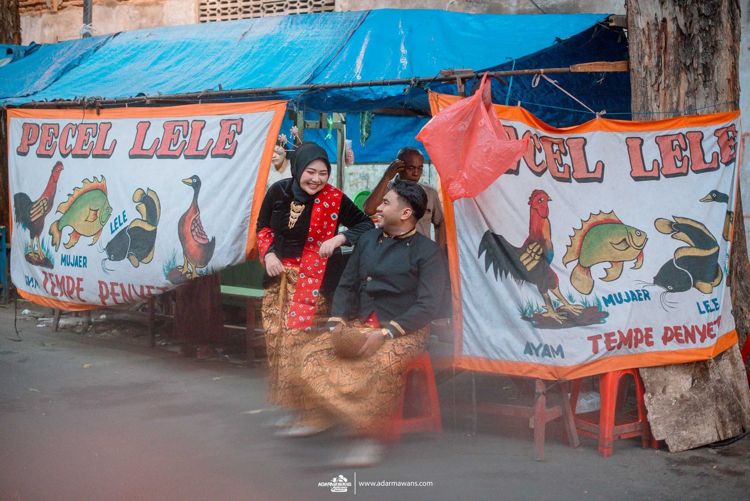 A street food stall with colorful banners and an awning advertising fried chicken against a rustic background.
