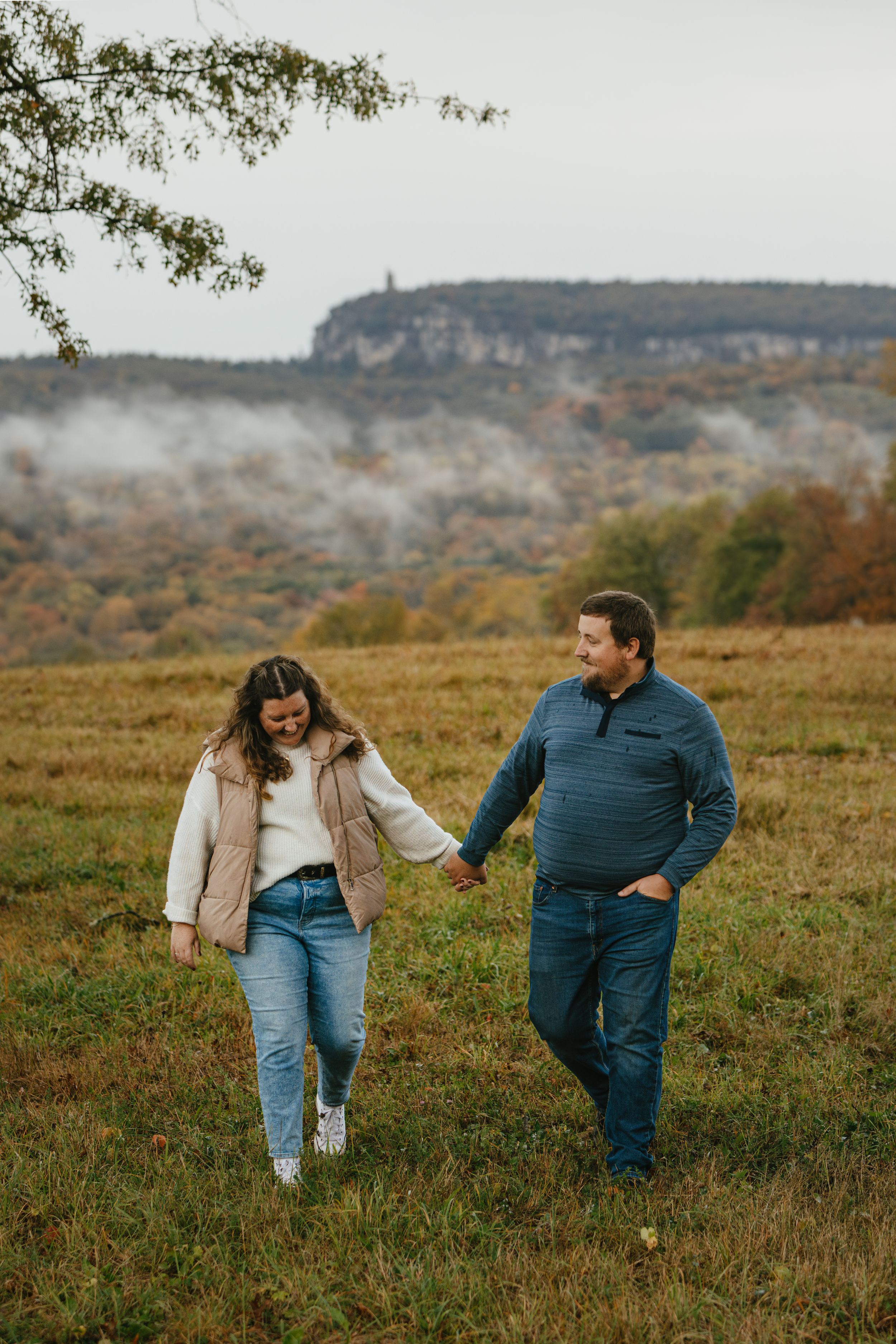 Three candid photos show a couple sharing laughter and playful moments in a scenic autumn field with hills in the background.