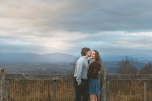 A couple shares an intimate moment against a scenic mountain landscape backdrop during sunset.