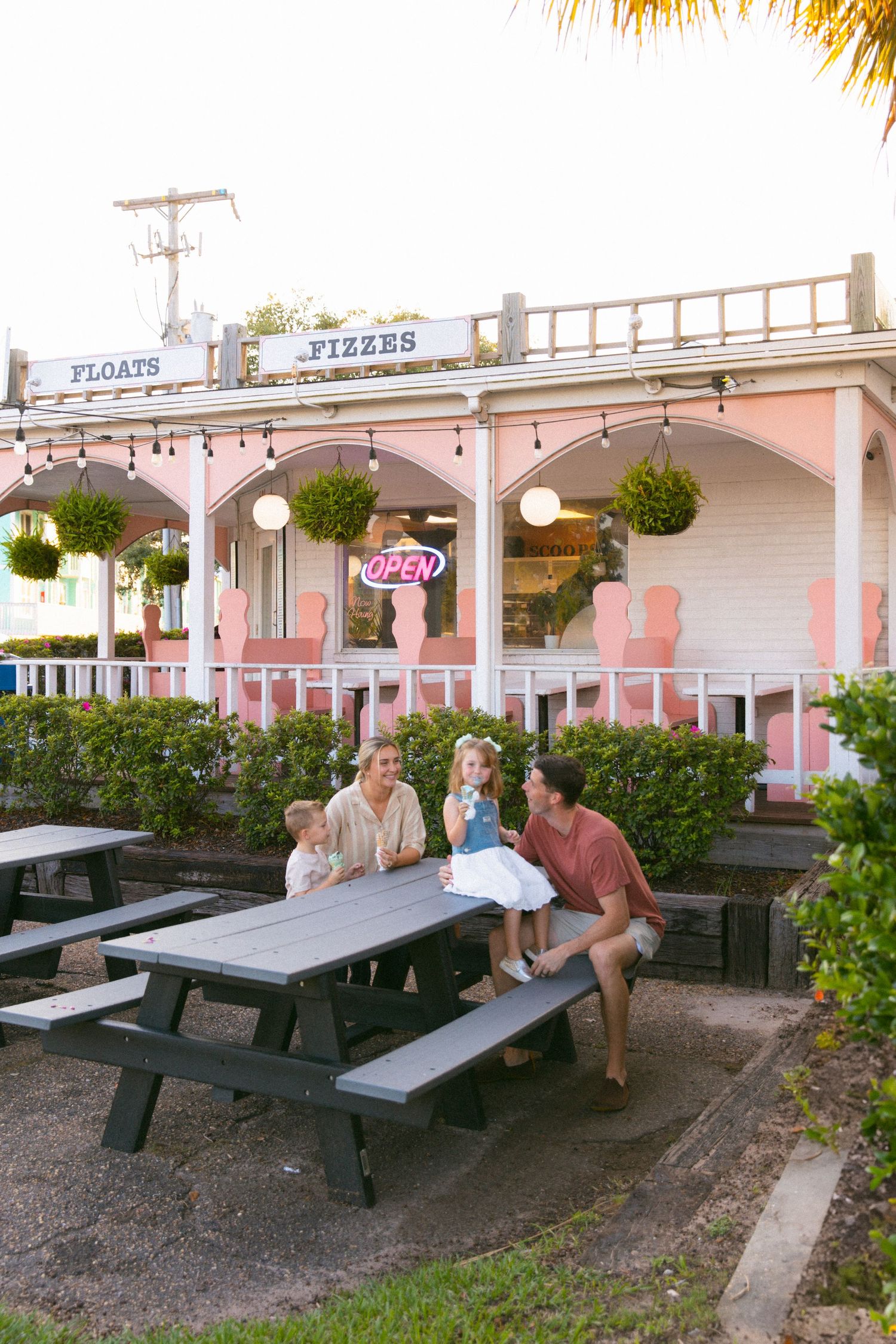 Family relaxing at outdoor seating area of pink-colored Fizzes storefront.