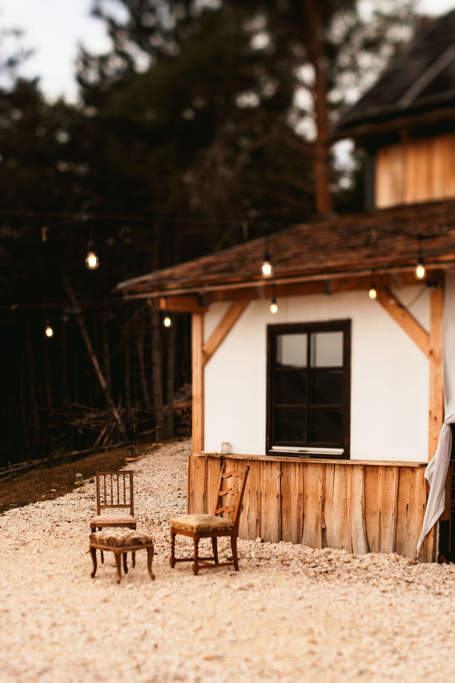 Rustic cabin exterior with wooden chairs and string lights creating cozy atmosphere.