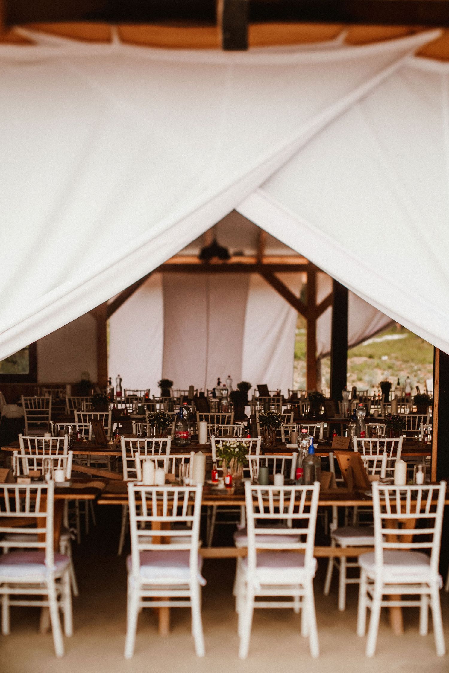 Wedding reception tent setup with rows of white chiavari chairs.