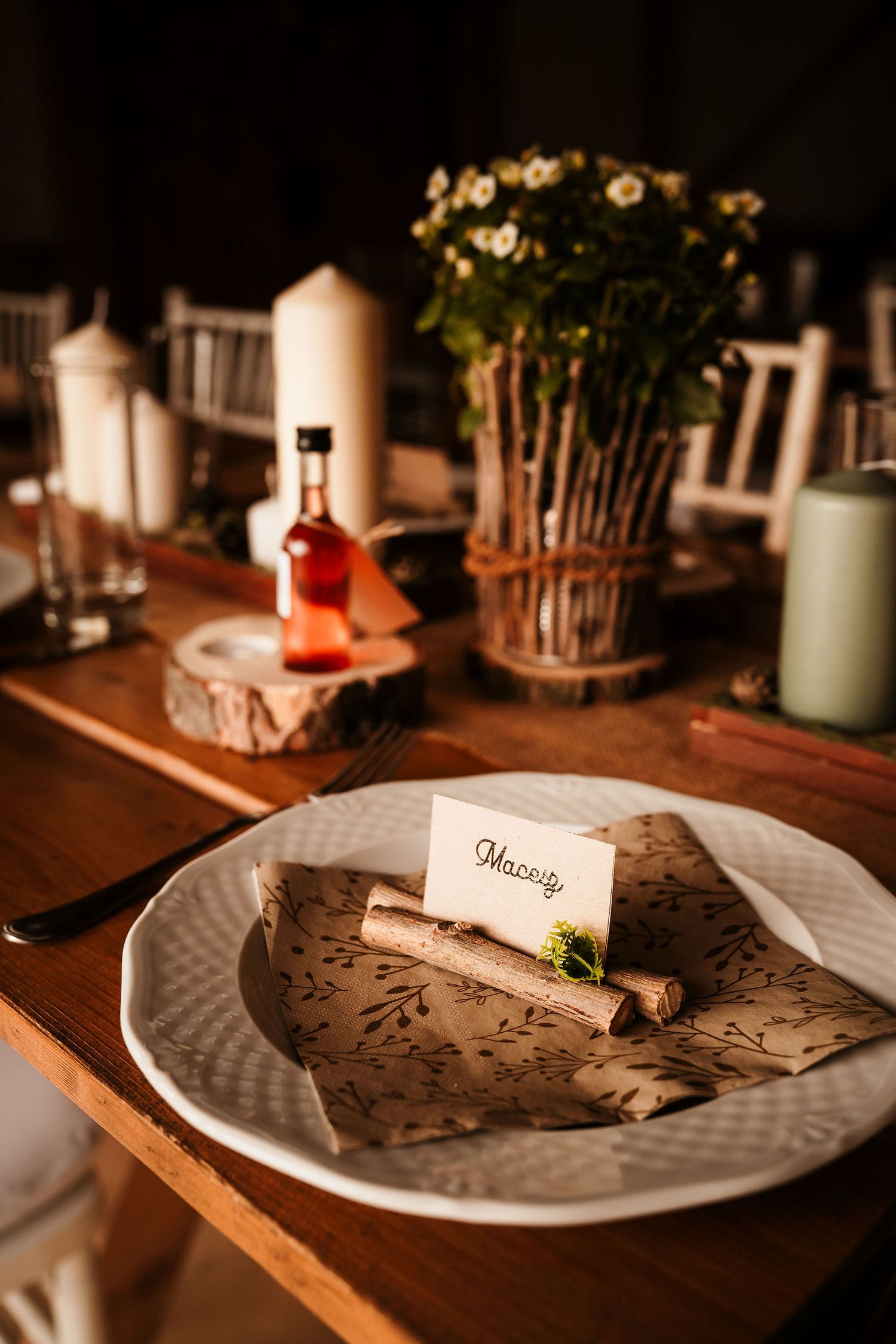 Wedding place setting with name card on rustic wooden plate and decorative candles.