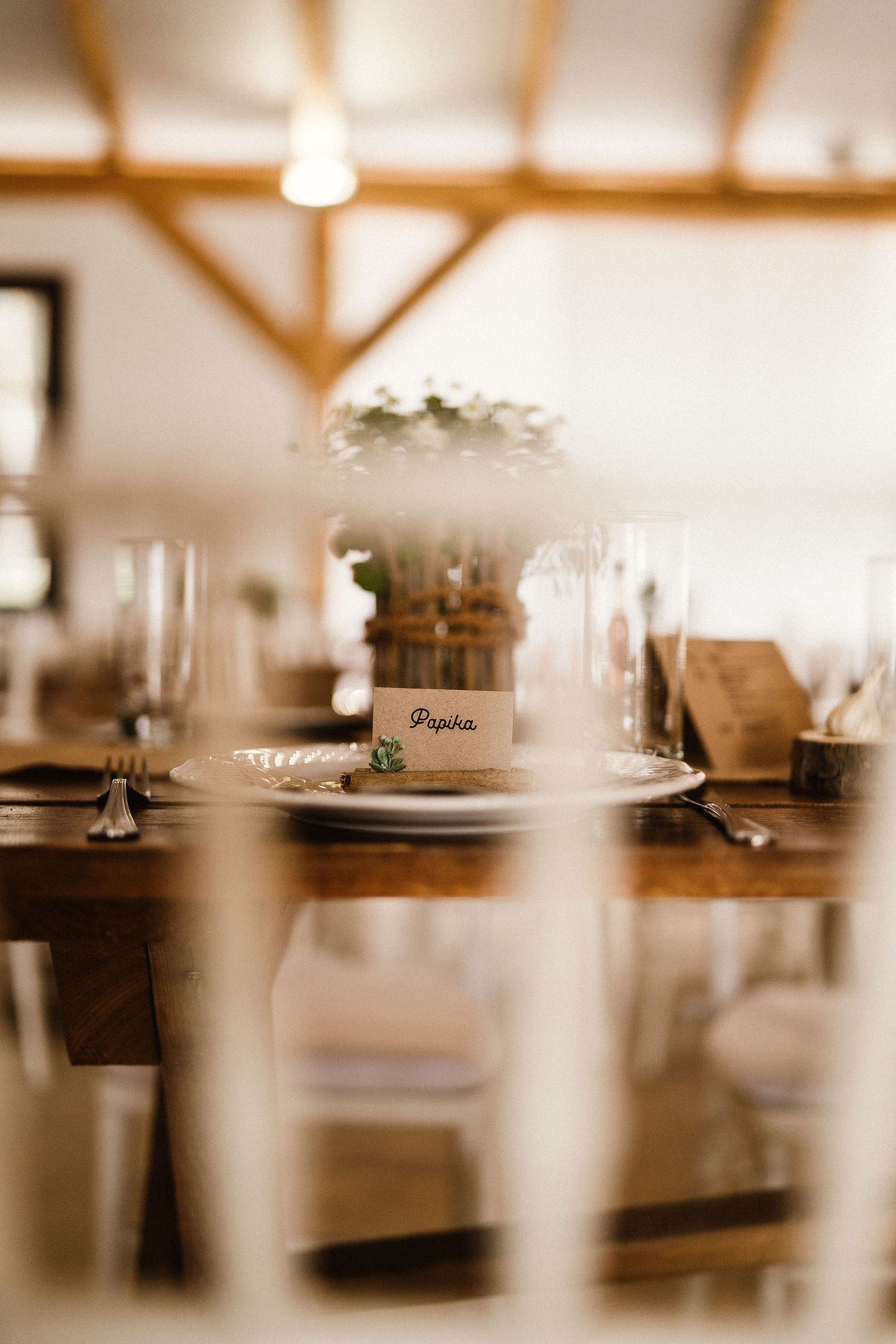 Place setting at rustic wedding reception with floral centerpiece and white chairs.